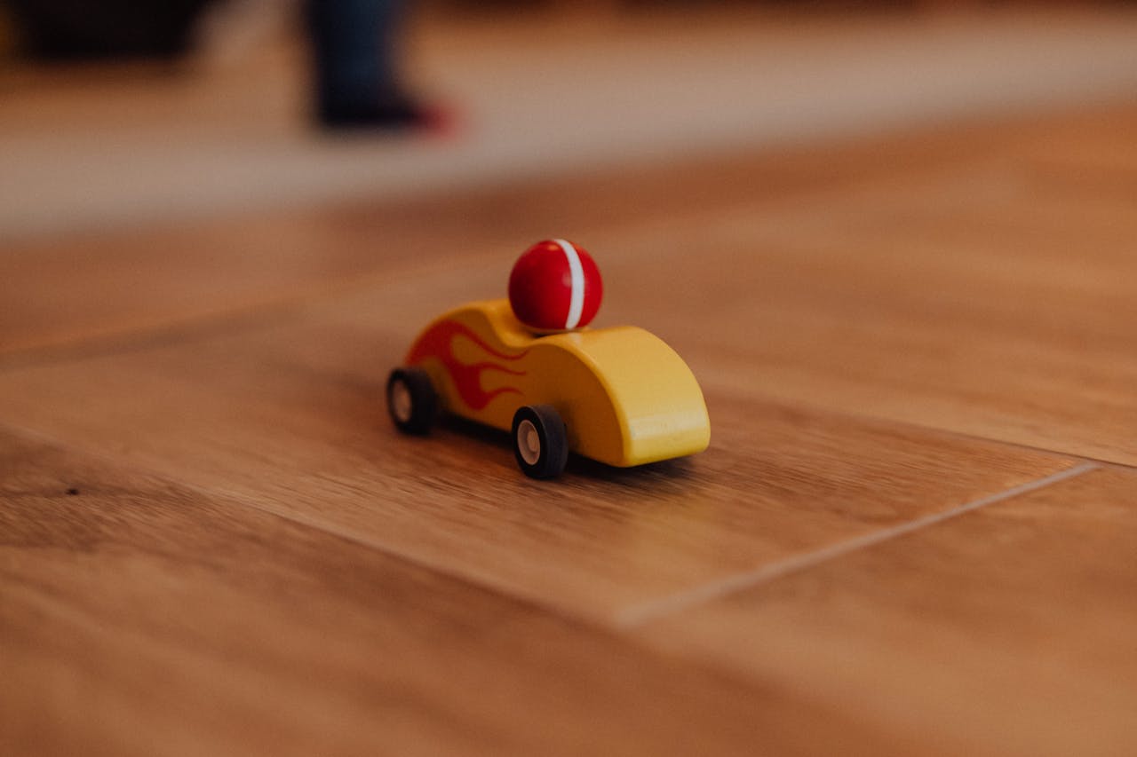 Close-up of a toy car with flames on a wooden floor, symbolizing childhood play.