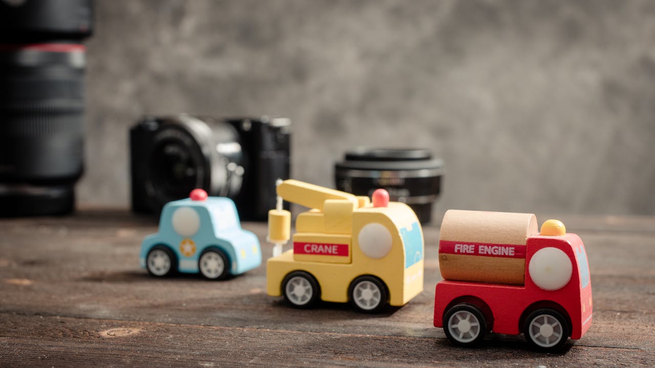 Close-up of colorful wooden toy vehicles on a wooden table with cameras in the background.
