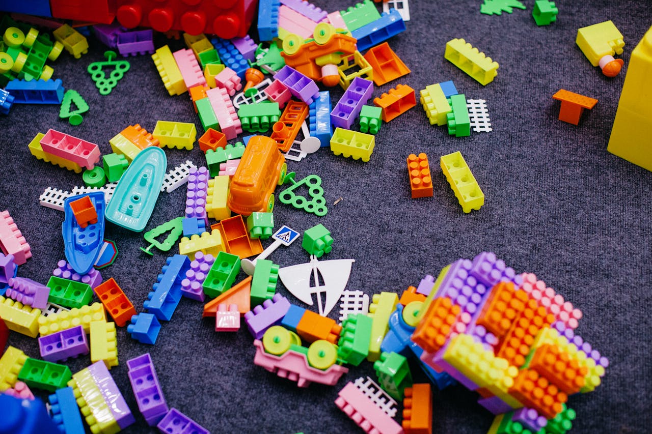 Vibrant plastic toy blocks scattered on a grey carpet, showcasing assorted shapes and colors.